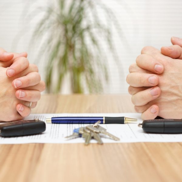 Two people's hands on a divorce document with keys, fobs, and a pen
