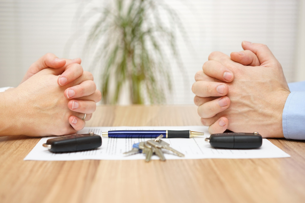 Two people's hands on a divorce document with keys, fobs, and a pen